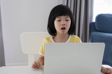 Küçük Asyalı kız öğrenci çevrimiçi evde dizüstü bilgisayar kullanıyor.