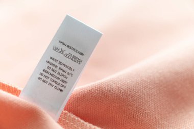 White laundry care washing instructions clothes label on pink cotton shirt