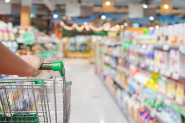 Bulanık süpermarket koridorlu alışveriş arabasını iten kadın.