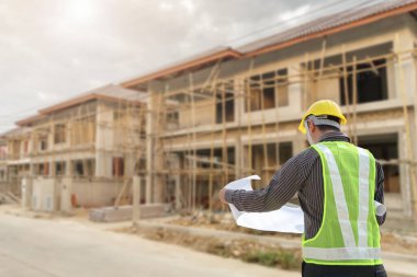 İnşaat şantiyesindeki koruyucu miğfer ve planlar üzerinde çalışan genç profesyonel mühendis.