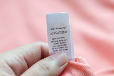 Beyaz çamaşırhanede el ele tutuşup kitap okuyoruz. Çamaşır yıkama talimatı. Pembe gömleğin üzerindeki kıyafet etiketi.
