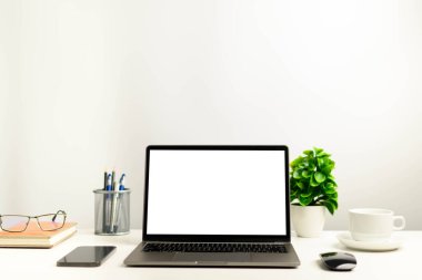 Teknoloji, defter, akıllı telefonlar, cihazlar kullanarak çalışan bir konsept. Ofisteki beyaz masadaki boş beyaz ekran dizüstü bilgisayar. Tasarım veya metin, Kapanış, Gri ve bulanık arkaplan için üstteki alanı kopyala