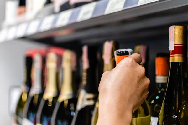 Kadın müşteri tutuyor, alışveriş merkezindeki kırmızı şarap şişesi etiketini seçiyor. Kadın marketin alkol reyonunda bir şişe şarap tutuyor. Raflar alkollü içeceklerle dolu. Bulanık arkaplan