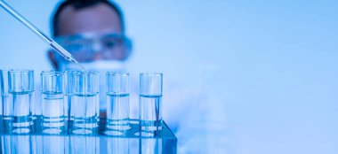 Koruyucu gözlük takan ve eldiven takan bir doktor aşıyı test etmek için kimyasallar damlatıyor. Biyokimyagerler yeni ilaçlar keşfetmek için deneyler yapıyorlar. Araştırmacılar bilim laboratuvarlarında çalışırlar.