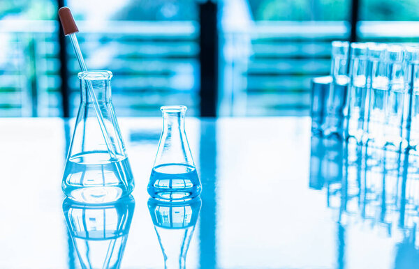 Chemistry experiment concept in science laboratory Two science flasks of different sizes contain different chemicals on white desk. nobody. Copy space on right for design. Blurred background. Close up