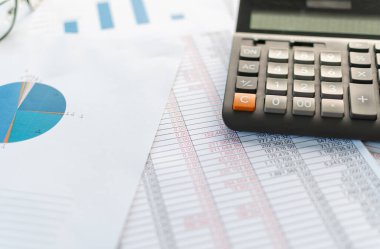 Finansal muhasebe, evden çalışma, masaüstü hesap makinesini kapatma, kağıt ve hesap makinesindeki hesap numarasını kontrol etme, bir sürü sayı, grafik, kağıt üzerinde gözlük, bulanık arkaplan