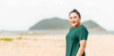 Sahilde durup gülümseyen ve kameraya bakan bir kadın. Açık deniz, hava açık. Tasarım veya içerik için sol taraftaki boşluğu kopyala. İnsanlar gülümser. Yaz, sıcak mevsim. Bulanık arkaplan