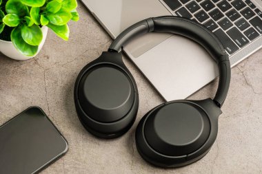 Akıllı bir telefonla müzik çalma, oturma odasında kablosuz kulaklıkla dinleme ve dinlenme kavramı. Yakın plan, seçici odaklanma. Gri bir masada siyah kulaklıklar. Bulanık arkaplan.