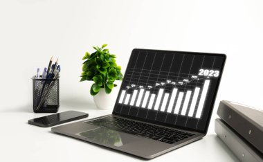 2023 yıllık grafik ofisteki beyaz bir masada dizüstü bilgisayarda gösteriliyor. 2023 yılında teknoloji, akıllı telefonlar, defterler, internet ve ekonomik büyüme kullanılarak yapılan iş kavramı yüksektir. Yakın plan..