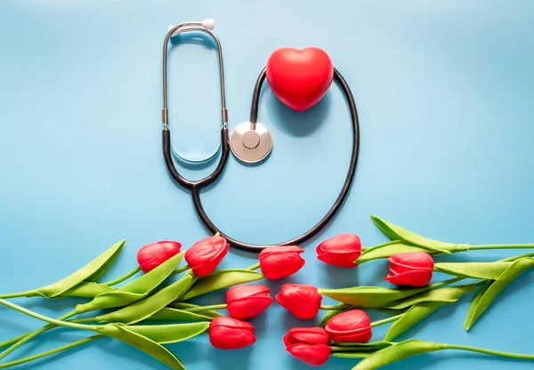 Greeting background. Happy nurse\'s day. Stethoscope, tulips, on blue background. Health day. National doctor\'s day. Top view, Closeup. Thank you, doctors and nurses