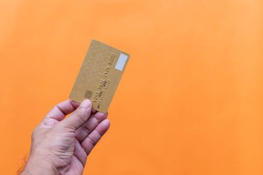 Close up, man's hand holding credit card on orange background. Businessman showing debit card online shopping, payment, online banking, money transfer, concept, selective focus, copy space on right.