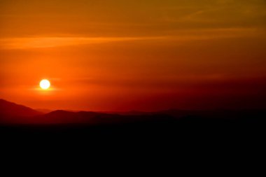 Güneş altın ışıkta batarken ve parktaki açık günün akşamında dağın tepesindeki parlak turuncu çember, gölgelerdeki evden gelen küçük bir ışık vardı. Sağda kopyalama alanı