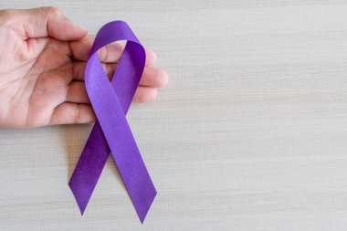 International Overdose Awareness Day, hand holds purple awareness ribbon on wooden table, a concept for World Lupus Day, Autoimmune disease, Immune System Disorders, May Lupus Awareness Month,