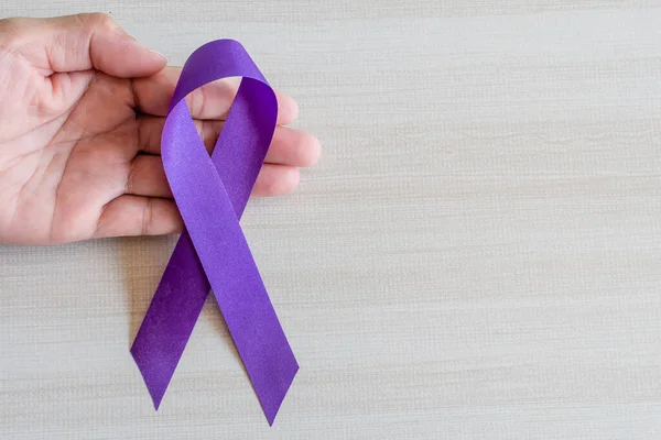 International Overdose Awareness Day, hand holds purple awareness ribbon on wooden table, a concept for World Lupus Day, Autoimmune disease, Immune System Disorders, May Lupus Awareness Month,