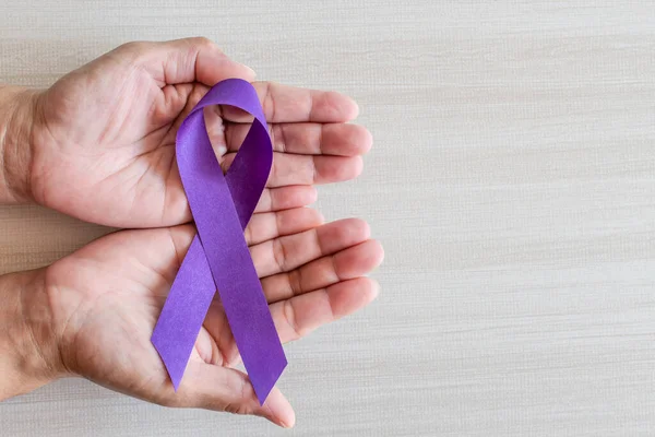 International Overdose Awareness Day, hand holds purple awareness ribbon on wooden table, a concept for World Lupus Day, Autoimmune disease, Immune System Disorders, May Lupus Awareness Month,