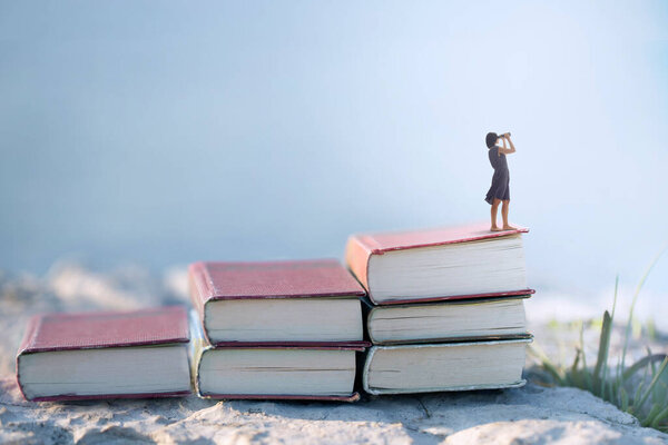 Woman with binoculars on the top of a ladder of books, surreal concept