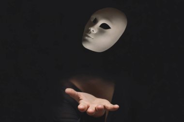Karanlıkta gizlenmiş bir insanın eli havaya bir maske fırlatıyor.