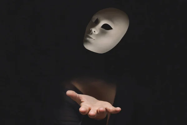 hand of a person hidden in the dark throwing a mask in the air