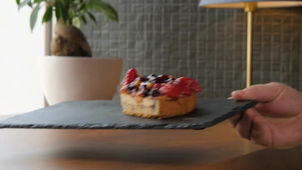 Die Hand legt einen Teller mit einem Stück Käsekuchen mit Beeren auf den Tisch — Stockvideo