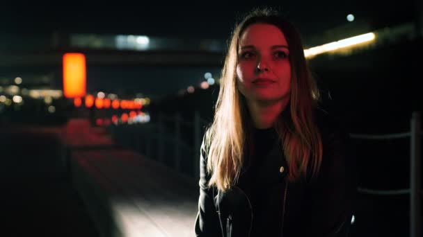 Portret van een mooie jonge vrouw zittend in een rood verlichte straat en glimlachend — Stockvideo