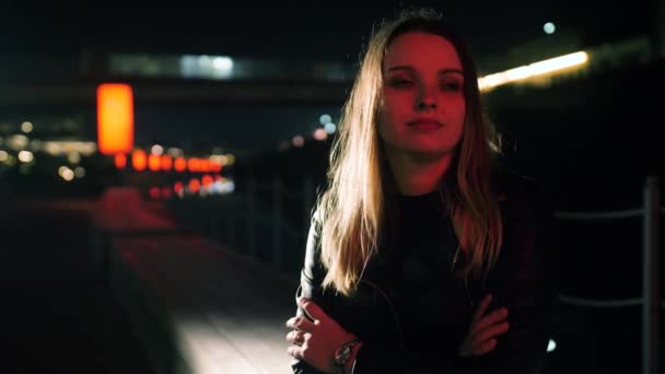 Porträtt av en söt ung kvinna som sitter på en bänk på en röd upplyst gata — Stockvideo