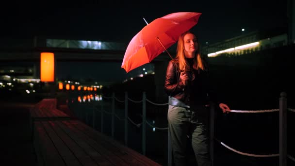 Hübsche junge Frau steht unter einem knallroten Regenschirm — Stockvideo