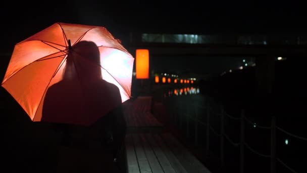 Silhueta de uma mulher em um guarda-chuva vermelho brilhante à noite — Vídeo de Stock