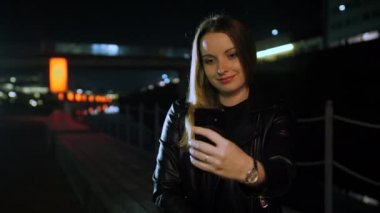 Kırmızı ışıklı bir sokakta oturan genç bir kadın akıllı telefondan selfie çekiyor.