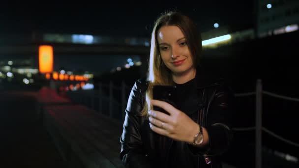 Jonge vrouw zitten op een rood verlichte straat het nemen van een selfie op een smartphone — Stockvideo