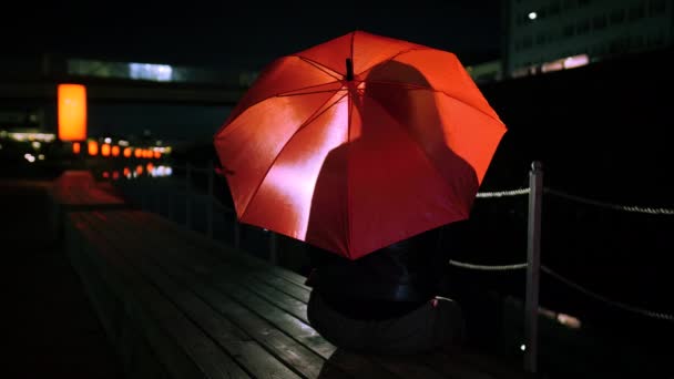 Frau sitzt auf Bank unter knallrotem Regenschirm — Stockvideo