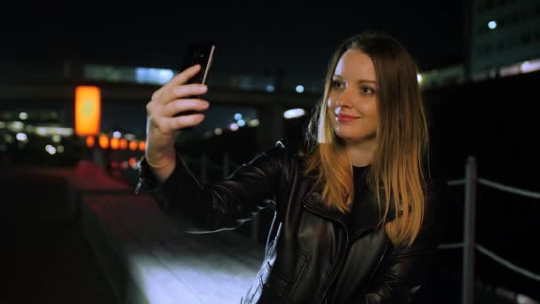 Jonge vrouw zitten op een rood verlichte straat het nemen van een selfie op een smartphone — Stockvideo