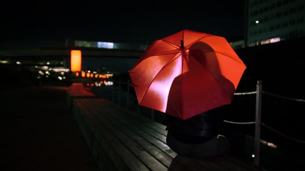 Femme est assise sur un banc sous un parapluie rouge vif — Video