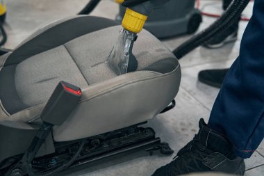 Otomobil tamircisi elektrikli süpürge kullanarak ön koltuğu temizliyor.