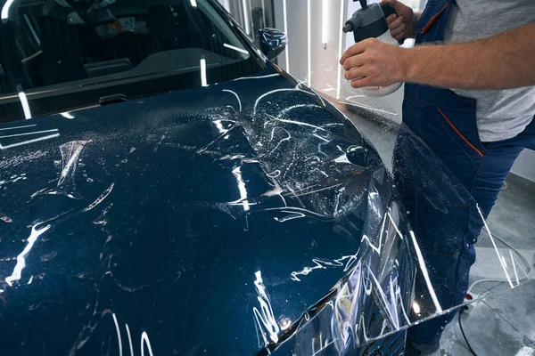 Autoservice-Spezialist sprüht Wasser auf Schutzlackfolie auf Motorhaube — Stockfoto