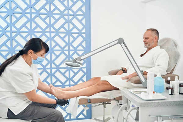 Pedicurist doet pedicure voor de mens in kosmetologie salon — Stockfoto
