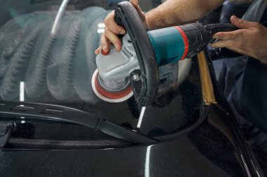 Tamirci, benzin istasyonunda araba cilası makinesi tutuyor.