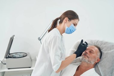 Tıbbi maskeli doktor alnına iğne yapıyor.