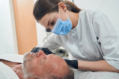 Kadın kozmetik uzmanı erkek yüzüne iğne yapıyor.