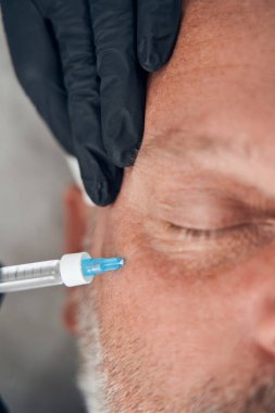 Doktor güzellik uzmanı elleri insan yüzüne iğne yapıyor.