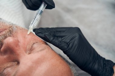 Adamın biri kozmetoloji kliniğinde yanağından iğne oluyor.