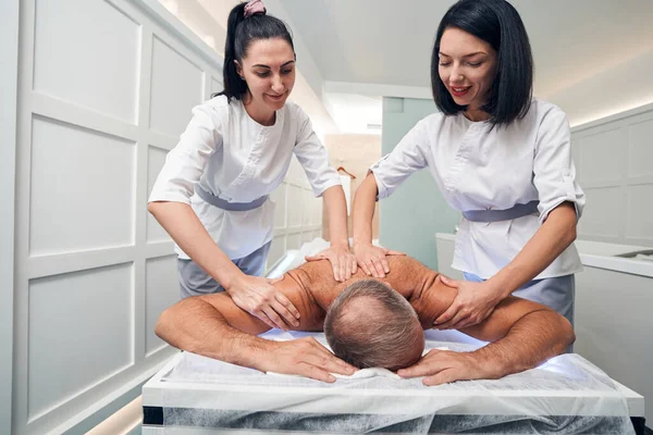 Massagistas sorridentes massageando homem de volta no salão de spa — Fotografia de Stock