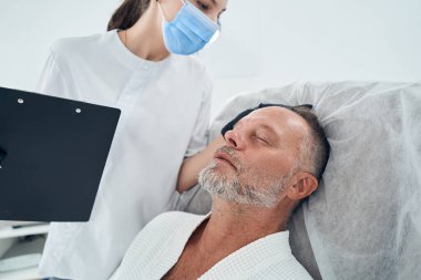 Doktor, kozmetoloji kliniğinde erkek saçını inceliyor.