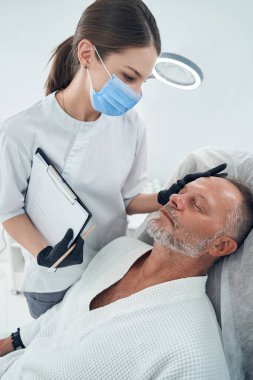 Güzellik uzmanı kozmetoloji kliniğinde erkek alnını inceliyor.