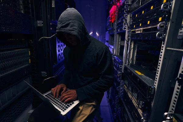 Focused hacker typing on laptop in server room