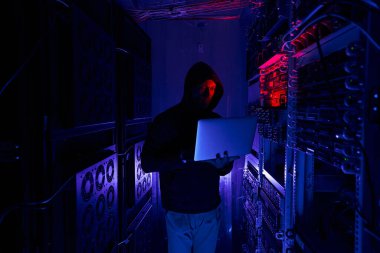 Karanlık sunucu odasında dizüstü bilgisayara odaklanmış hacker.