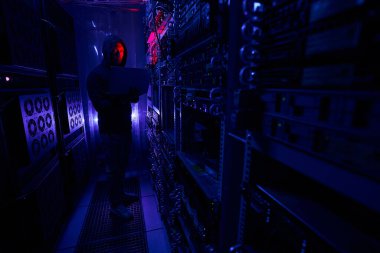 Karanlık sunucu odasında elinde laptop olan bir bilgisayar korsanı.