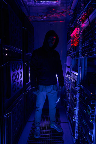 Male hacker in hoodie among server racks