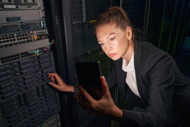 Cep telefonu kullanarak veri merkezinde çalışan genç bir kadın.