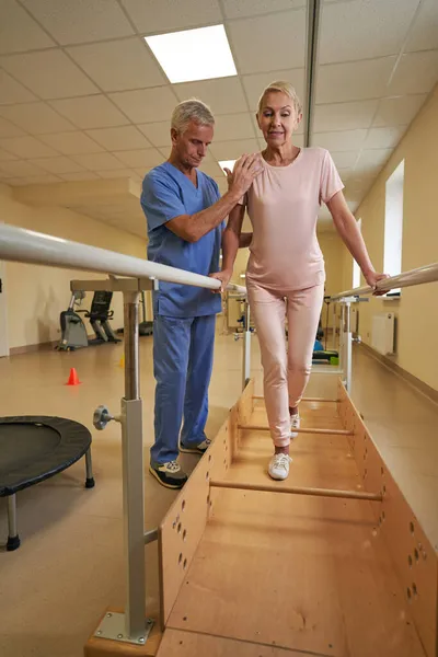Kadın hasta rehabilitasyon merkezinde yürümek için paralel barlar kullanıyor. — Stok fotoğraf