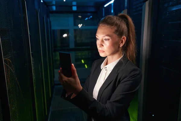 Técnico femenino trabaja en celular en centro de datos — Foto de Stock